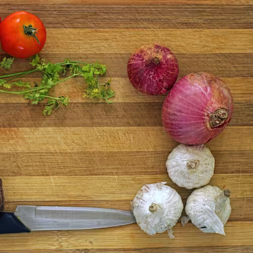 Fresh ingredients including tomato, onions, and garlic arranged on a cutting board with a kitchen knife.